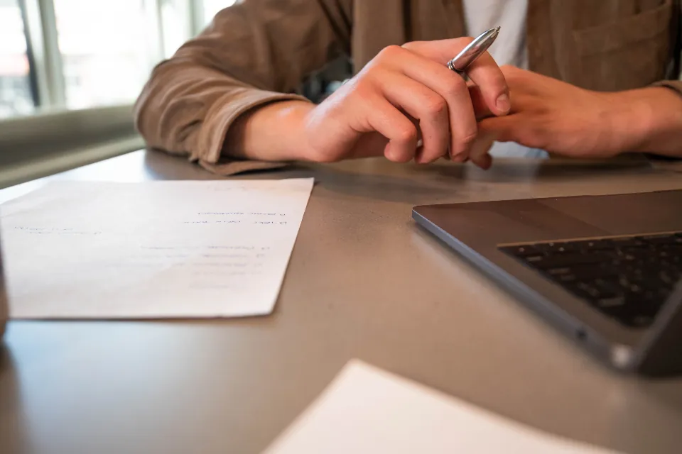 Person mit Stift über Dokumenten am Schreibtisch